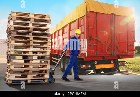 Arbeiter, der Holzpaletten mit Handgabelstapler und modernem Lkw im Freien bewegt Stockfoto