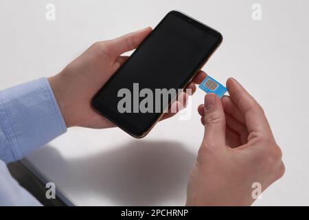 Frau mit SIM-Karte und Smartphone am weißen Tisch, Nahaufnahme Stockfoto