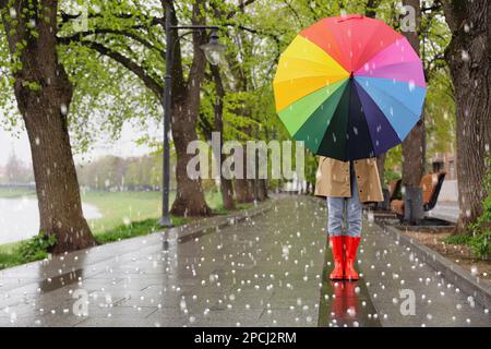 Junge Frau mit Regenschirm, die an regnerischen Tagen im Park spaziert und gegrüßt wird Stockfoto