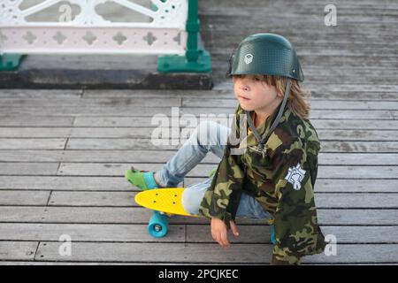 Ein Junge sitzt auf einem gelben Skateboard Stockfoto