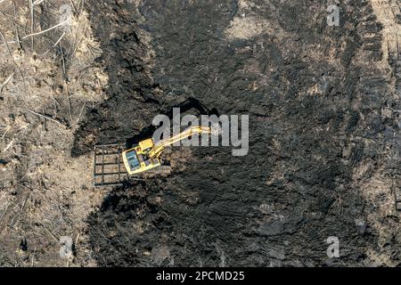 Gelber Arbeitsbagger zum Graben von schwarzem Boden oder Torf. Draufsicht von oben von der fliegenden Drohne. Stockfoto