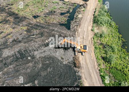 Großer Industriebagger, der an sonnigen Tagen in Sumpfgebieten arbeitet. Luftaufnahme von der fliegenden Drohne. Stockfoto