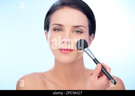 Rosige Wangen kreieren. Eine junge Frau, die Rouge mit einem Make-up-Pinsel aufträgt. Stockfoto