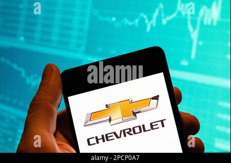 China. 15. Februar 2023. In dieser Fotoabbildung wird das Logo der amerikanischen Automobilmarke General Motors (GM), Chevrolet, auf einem Smartphone mit einer Grafik des Börsenindex im Hintergrund angezeigt. Kredit: SOPA Images Limited/Alamy Live News Stockfoto