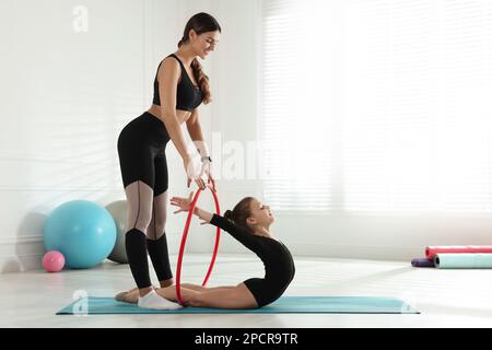 Der Turntrainer hilft kleinen Mädchen, sich mit dem Reifen drinnen zu dehnen Stockfoto