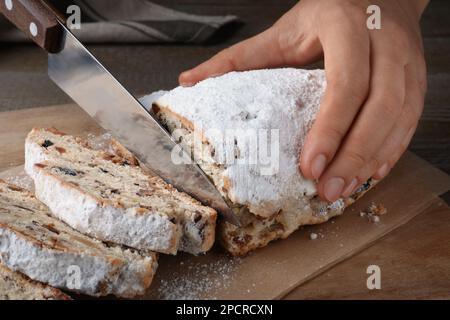 Frau schneidet traditionelle Weihnachtsstollen auf Holzbrett, Nahaufnahme Stockfoto