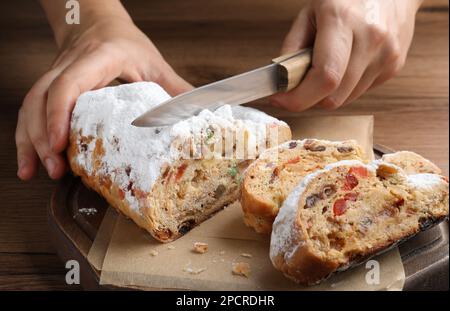 Eine Frau schneidet traditionelle Weihnachtsstollen auf einem Holztisch, Nahaufnahme Stockfoto