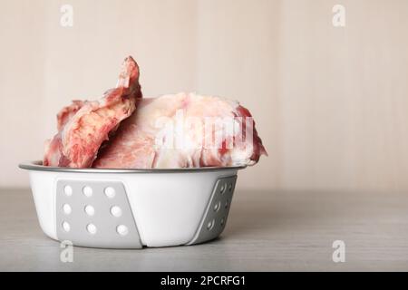 Fütterschüssel mit rohen Fleischknochen auf weißem Holztisch. Platz für Text Stockfoto