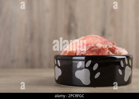 Fütterschüssel mit rohen Fleischknochen auf Holztisch. Platz für Text Stockfoto