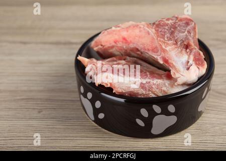 Fütterschüssel mit rohen Fleischknochen auf Holztisch. Natürliches Tierfutter Stockfoto