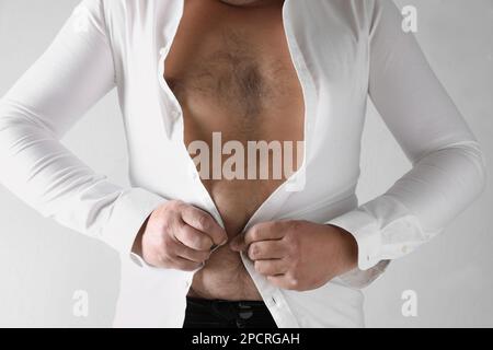 Ein Mann, der versucht, ein enges Hemd auf hellem Hintergrund zuzuknöpfen, Nahaufnahme. Übergewichtigkeitsproblem Stockfoto