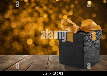 Wunderschöne Geschenkbox auf Holztisch gegen verschwommene festliche Lichter, Bokeh-Effekt. Platz für Text Stockfoto