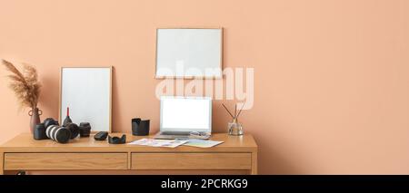 Arbeitsplatz des Fotografen mit Laptop, modernen Geräten und leeren Rahmen nahe beigefarbener Wand. Banner für Design Stockfoto
