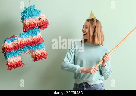 Junge Frau bricht mexikanische Pinata auf grünem Hintergrund Stockfoto