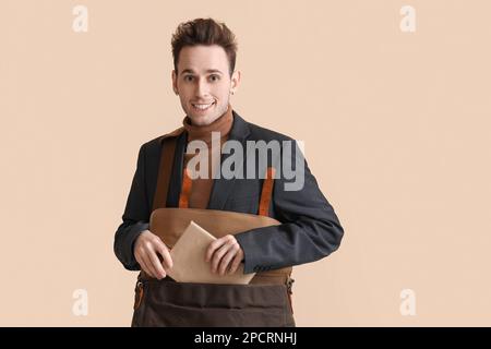 Junger Mann, der ein Buch auf beigefarbenem Hintergrund in eine Tasche steckt Stockfoto