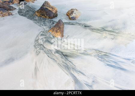 Natürliche Muster entstehen am weißen Sandstrand von Stewart Island, Neuseeland, während Süßwasser an den Strand fließt und einen alluvialen Fan bildet. Stockfoto