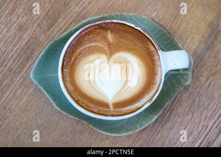 Heißer Cappuccino-Kaffee mit herzförmiger Latte Art auf einem Holztisch Stockfoto