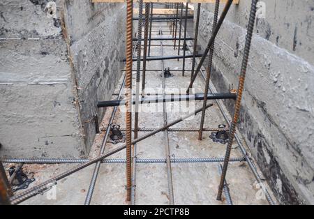 Eine Nahaufnahme einer Hausgrundkonstruktion mit Holzrahmen und montierten Bewehrungsbügeln und gegossenem Beton. Aufbau eines Fundaments aus Stahlbeton. Stockfoto