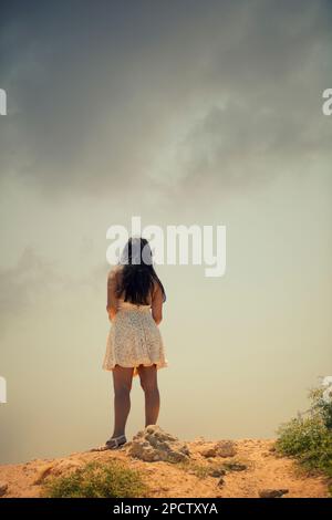 Rückansicht einer Frau in einem kurzen weißen Kleid, die draußen steht Stockfoto