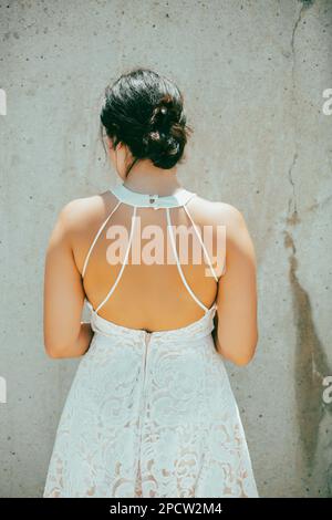 Rerar-Blick auf eine Frau in weißem Kleid, die draußen an der Wand steht Stockfoto