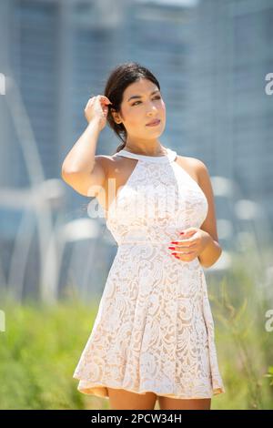 Schöne junge Frau in weißem Kleid, die draußen steht und wegschaut Stockfoto