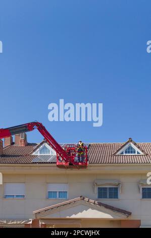 Arbeiter, die Solarpaneele auf dem Dach eines Terrassenhauses installieren. Sie arbeiten über dem Gelenkausleger Stockfoto