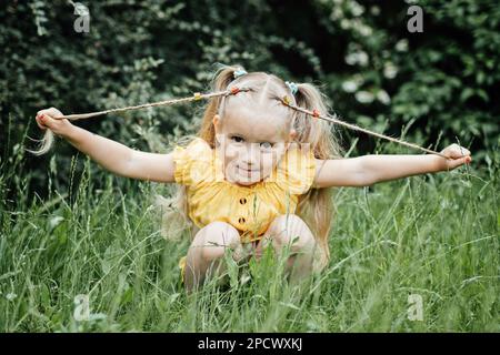 Sommeraktivitäten und Verbindung mit der Natur für Kinder. Süßes kleines Mädchen mit zwei Pferdeschwänzen läuft, tanzt und spielt auf dem grünen Rasen Stockfoto