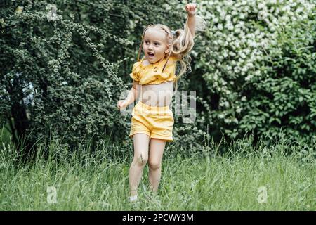 Sommeraktivitäten und Verbindung mit der Natur für Kinder. Süßes kleines Mädchen mit zwei Pferdeschwänzen läuft, tanzt und spielt auf dem grünen Rasen Stockfoto