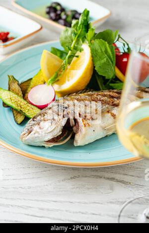 Gegrillte Meerbrasse mit Gemüse und Grün auf einem Holztisch Stockfoto