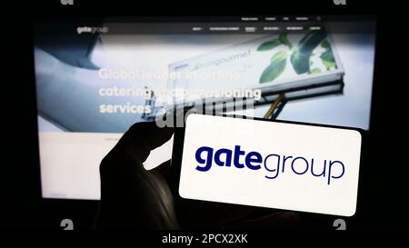 Person, die ein Mobiltelefon mit dem Logo der Schweizer Gategroup Holding AG auf dem Bildschirm vor der Webseite hält. Konzentrieren Sie sich auf das Display des Telefons. Stockfoto