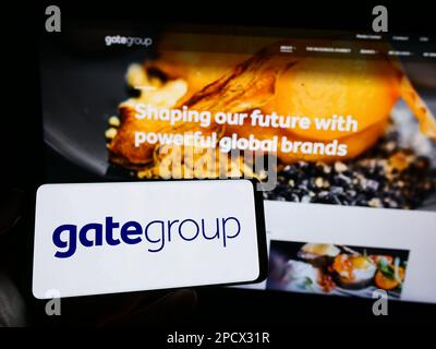 Person, die ein Handy mit Logo der Schweizer Gategroup Holding AG auf dem Bildschirm vor der Webseite hält. Konzentrieren Sie sich auf das Display des Telefons. Stockfoto