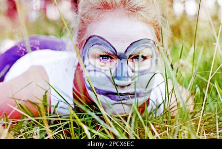 Umea, Norrland Schweden - 22. August 2005: Junge Frau hat sich als Frosch gemalt und liegt im Gras Stockfoto