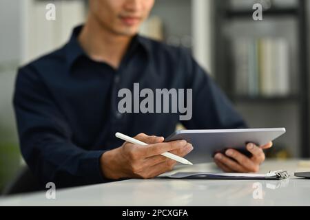 Selektive Fokussierung auf die Hände. Zugeschnittenes Bild eines Geschäftsmanns, der einen Stift hält und ein digitales Tablet am Schreibtisch verwendet Stockfoto