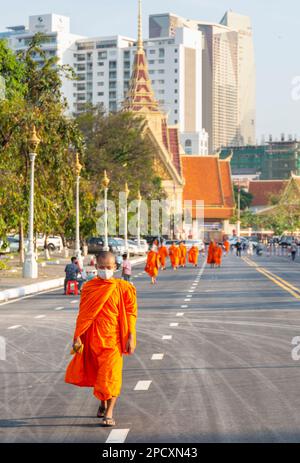 Phnom Penh, Kambodscha-Dezember 23 2023: Gekleidet in traditionellen orangefarbenen Bademänteln, Mönche, viele tragen Gesichtsmasken, machen Sie einen Spaziergang vorbei am Royal Palace Park, auf einem breiten Ro Stockfoto