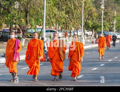 Phnom Penh, Kambodscha-Dezember 23 2023: Gekleidet in traditionellen orangefarbenen Bademänteln, Mönche, viele tragen Gesichtsmasken, machen Sie einen Spaziergang vorbei am Royal Palace Park, auf einem breiten Ro Stockfoto