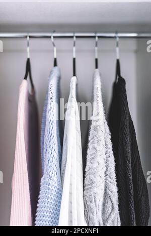 Minimalistische Kapselgarderobe Auswahl an Damenmode Pullover und Strickjacken hängen an Kleiderstange mit passenden Kleiderbügeln, die bei geringer Schärfentiefe aufgenommen werden Stockfoto