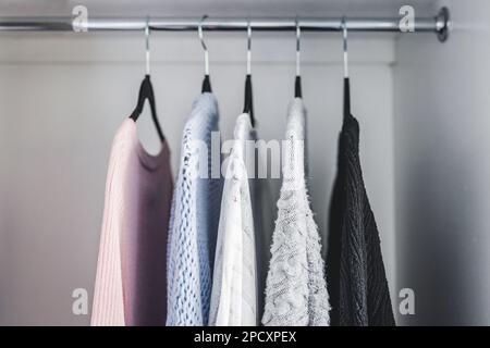 Minimalistische Kapselgarderobe Auswahl an Damenmode Pullover und Strickjacken hängen an Kleiderstange mit passenden Kleiderbügeln, die bei geringer Schärfentiefe aufgenommen werden Stockfoto