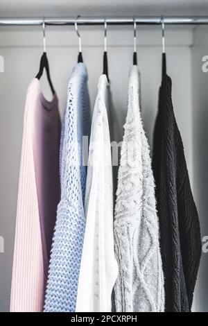 Minimalistische Kapselgarderobe Auswahl an Damenmode Pullover und Strickjacken hängen an Kleiderstange mit passenden Kleiderbügeln, die bei geringer Schärfentiefe aufgenommen werden Stockfoto