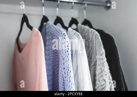 Minimalistische Kapselgarderobe Auswahl an Damenmode Pullover und Strickjacken hängen an Kleiderstange mit passenden Kleiderbügeln, die bei geringer Schärfentiefe aufgenommen werden Stockfoto