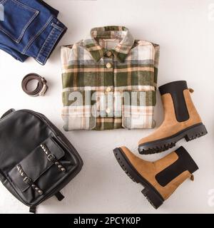 Kleidung. Kariertes Hemd, Jeans, beige Stiefel, Lederrucksack. Schuhe und Kleiderschrank. Moderner Style für Damen. Draufsicht der Kleidung. Damenbekleidung und Accessoires Freizeit Frühling Winter Herbst Outfit. Stockfoto