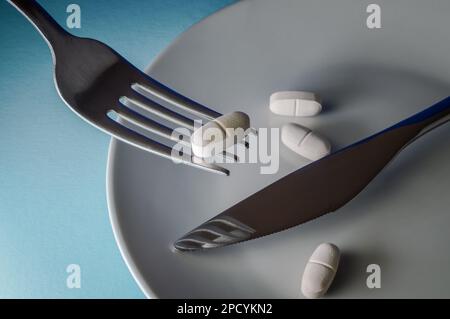 Gabel hält eine Medizinpille auf blauem Hintergrund - Konzept für Essstörungen, Medikamentenmissbrauch, chemische Ernährung, Gesundheitsprobleme Stockfoto