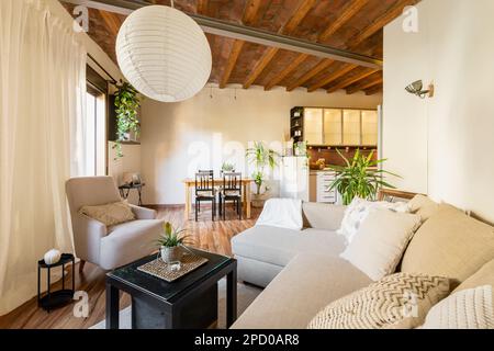 Kleines Wohnzimmer mit neuen Sofalampen und Couchtisch mit Blick auf den Küchenbereich und Holzbalkendecke im Studio-Apartment mit vielseitigem Ambiente Stockfoto