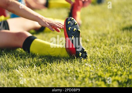 Fußballspieler, Der Sich Die Beine Streckt. Fußballspieler in Fußballschuhen macht Stretching-Übungen während des Sporttrainings auf dem Fußballplatz Stockfoto