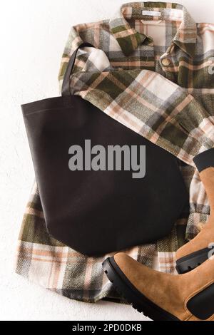 Schwarze umweltfreundliche Einkaufstasche mit Platz für Text. Bag-Modell-Vorlage, Draufsicht. Kleiderschrank mit Hemd und Stiefeln. Kleidung und Accessoires. Moderne Accessoires. Unisex-Karohemd Stockfoto