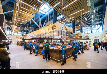 Verschiedene Fischstände, besetzt von Verkäufern in blauen Uniformen. Bei der Fischmarktgenossenschaft in Abu Dhabi, Vereinigte Arabische Emirate. Stockfoto