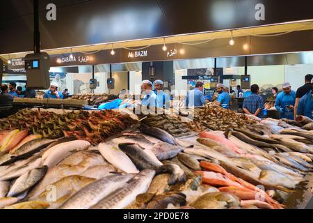 Verschiedene Fischstände, besetzt von Verkäufern in blauen Uniformen. Bei der Fischmarktgenossenschaft in Abu Dhabi, Vereinigte Arabische Emirate. Stockfoto