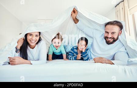 Familie, Porträt und Decke im Bett mit Kindern und Eltern, glücklich und spielend zu Hause. Gesicht, Unterwäsche und Bettlaken von Kindern mit mom und Dad Stockfoto