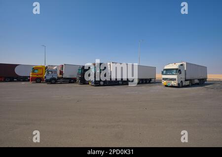 Große Sattelschlepper stehen in Schlange und parken an einer der anderen Haltestellen. Abseits der Autobahn E11 vor Abu Dhabi, Vereinigte Arabische Emirate. Stockfoto