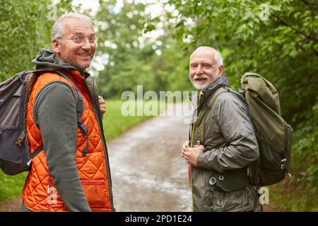 Porträt lächelnder männlicher Freunde mit Rucksäcken, die während des Urlaubs den Wald erkunden Stockfoto