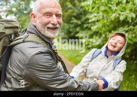 Porträt eines sorgenfreien älteren Paares in Jacken, das zusammen im Urlaub im Wald wandert Stockfoto